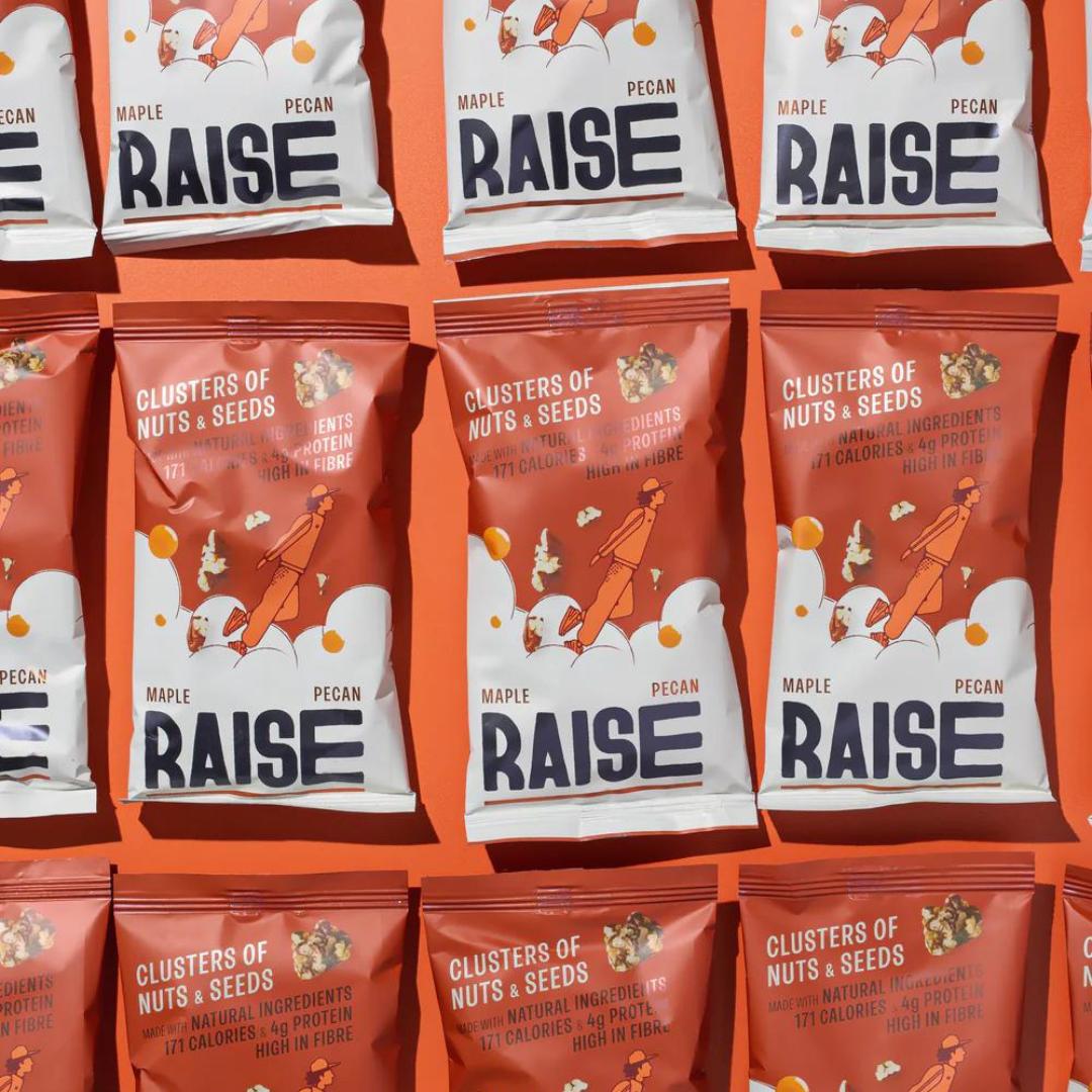 Multiple red and white Raise Snacks Maple Pecan pouches with a person climbing a nut tree design.