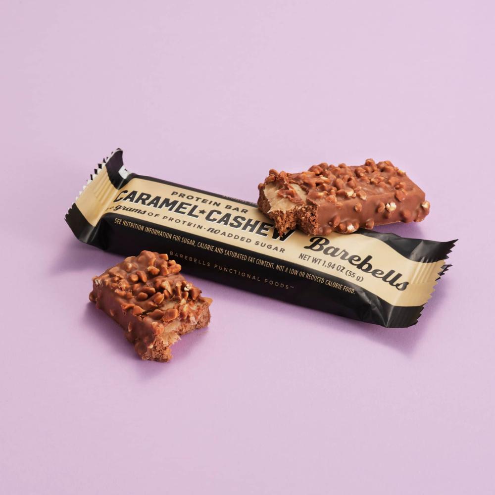 Barebells Caramel Cashew protein bar, unwrapped and bitten, showing gooey caramel and cashew chunks in milk chocolate.