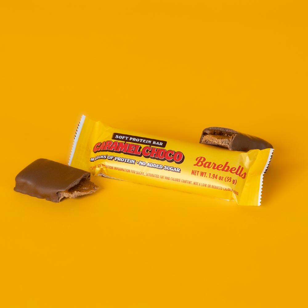 Barebells Caramel Choco soft protein bar, partially unwrapped, showing milk chocolate coating and caramel filling.