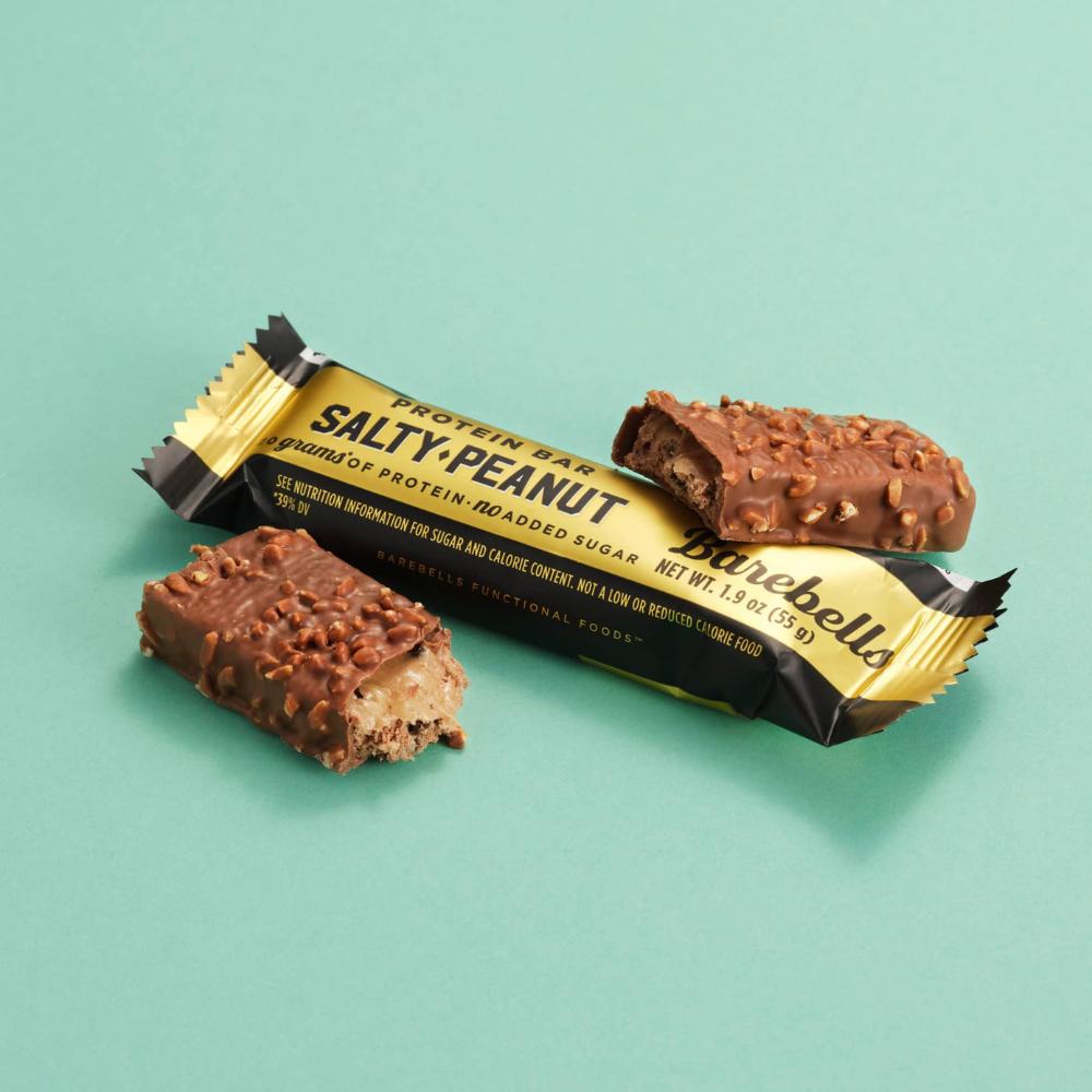 Barebells Salty Peanut protein bar, unwrapped and broken, revealing milk chocolate and peanuts.