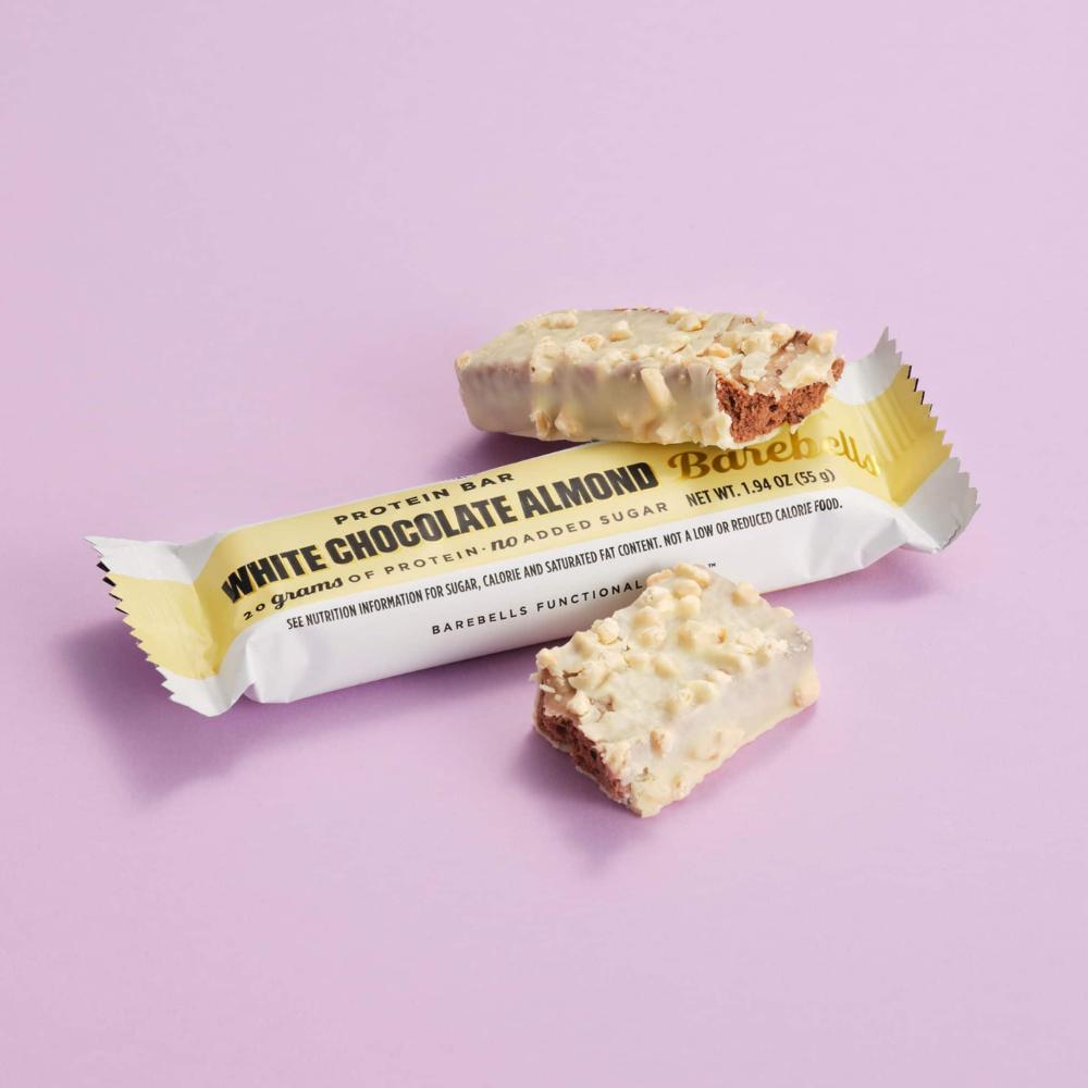 Barebells White Chocolate Almond protein bar, unwrapped with a bite taken, showing caramel and almond pieces.