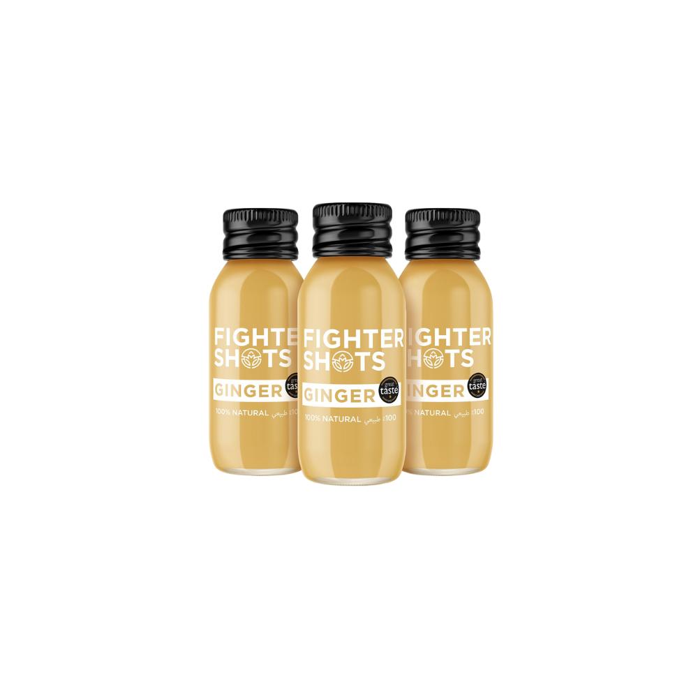 Three small, clear glass bottles of Fighter Shots Ginger juice with black caps and white labels.