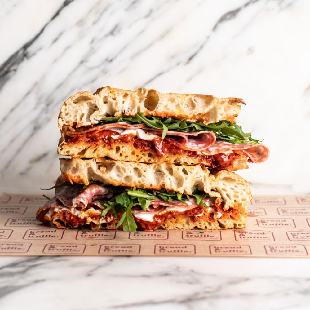 Stacked focaccia sandwich with spicy salami, red nduja spread, creamy ricotta, and fresh rocket.