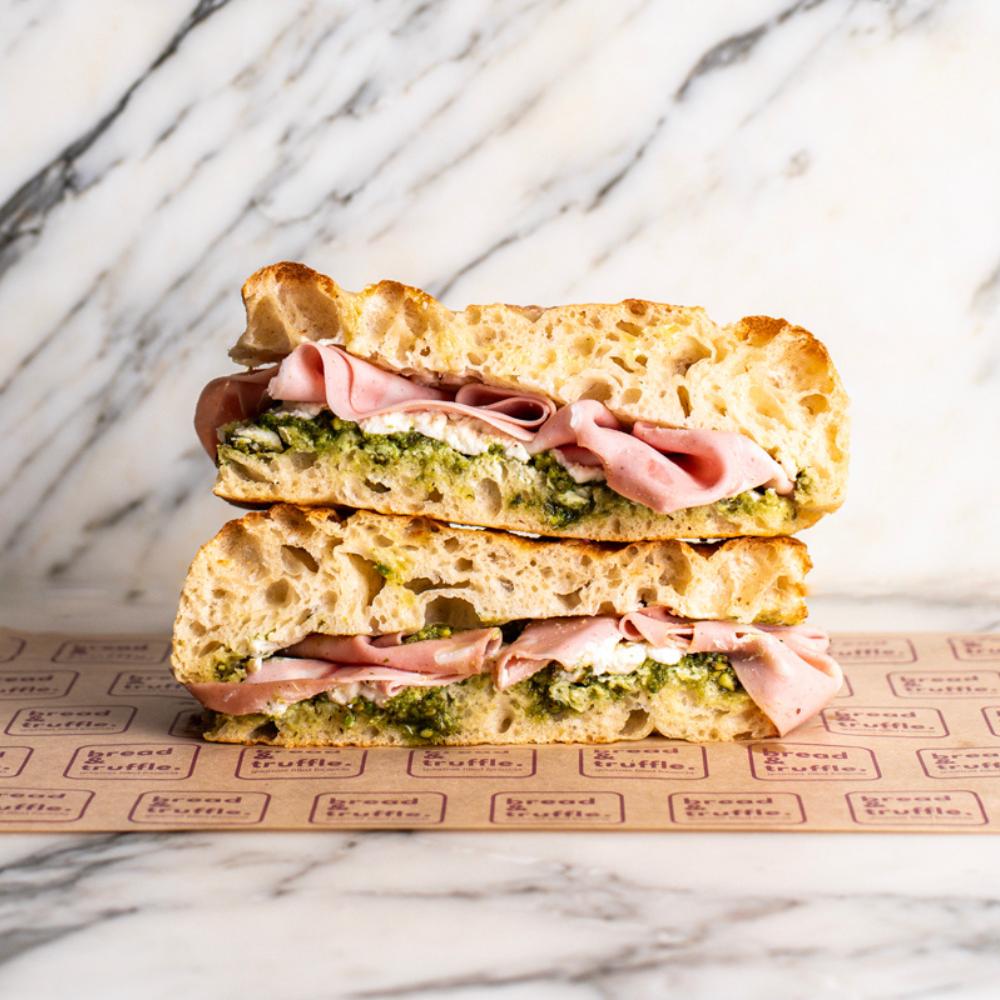 Focaccia Nutty Ham sandwich with mortadella, ricotta, and pistachio pesto on marble.