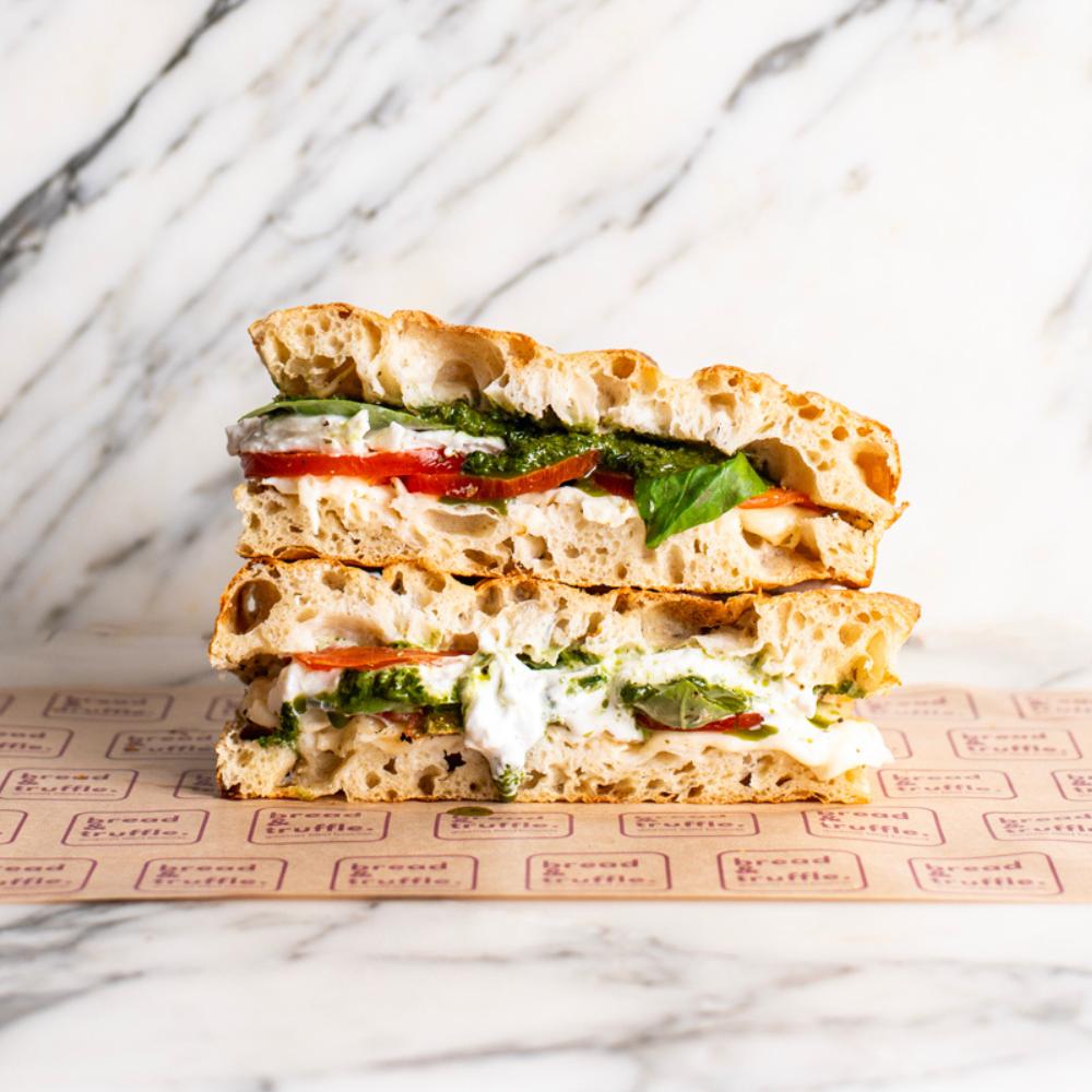 Twisted Caprese Focaccia Sandwich with fresh mozzarella, red tomatoes, green basil pesto, and basil leaves.