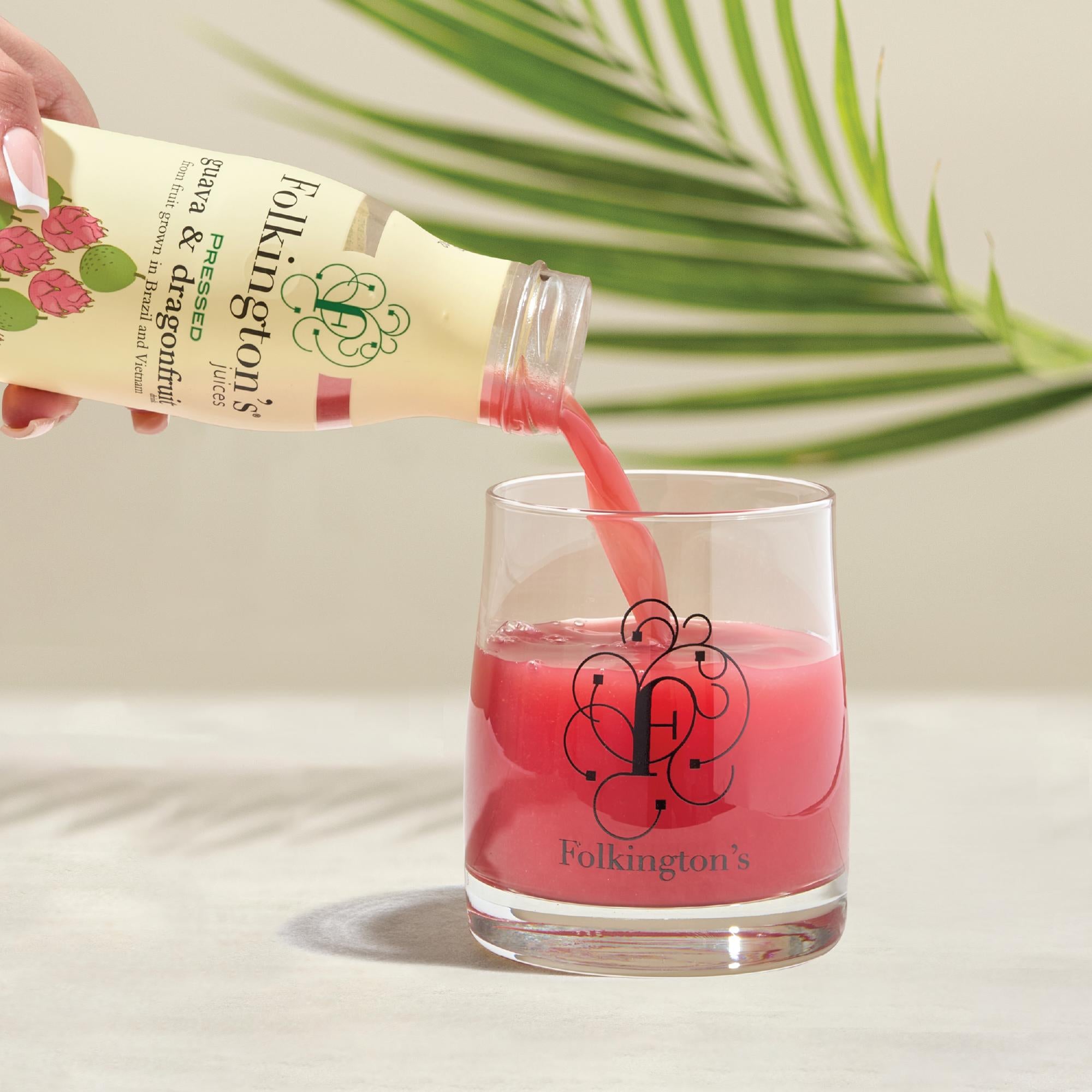 Folkington's Pressed Guava & Dragon Fruit Juice pouring into a branded glass, with a palm leaf background.