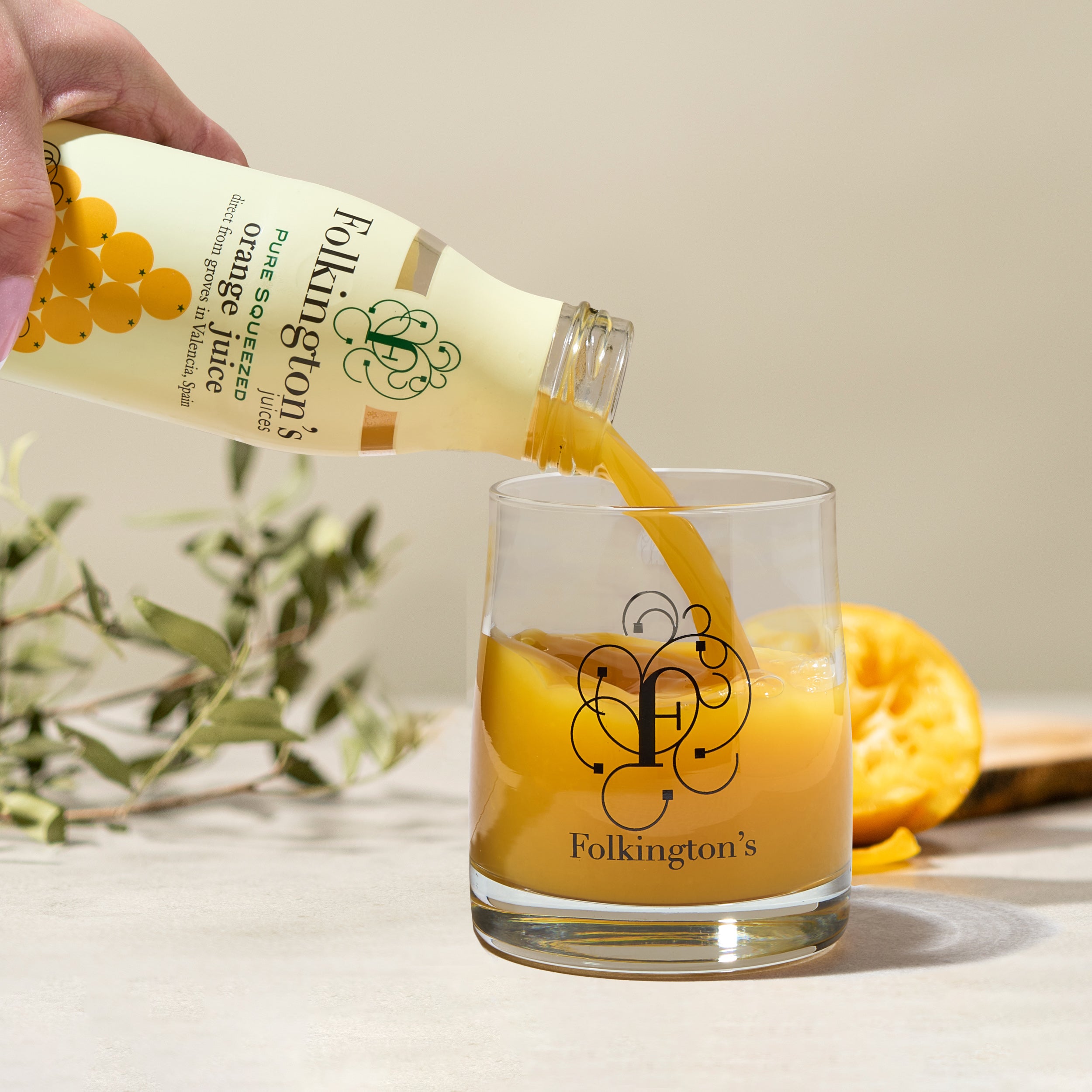 Hand pouring Folkington's Pure Squeezed Orange Juice from a 250ml bottle into a branded glass.