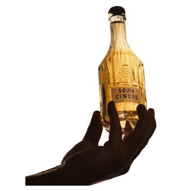 Hand holding a clear, textured glass Soba Circus sparkling nootropic drink bottle with a black cap.