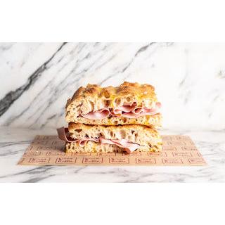 Focaccia mortadella & taleggio sandwich, stacked on brown paper, against a marble background.
