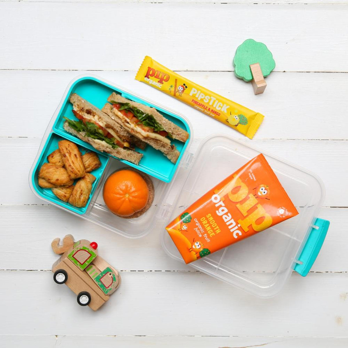 Pip Organic Smooth Orange Juice carton, a lunchbox with sandwiches, pastries, an orange, and a Pipstick.