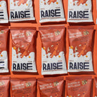 Multiple red and white Raise Snacks Maple Pecan pouches with a person climbing a nut tree design.