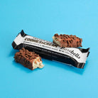 Barebells Cookies & Cream protein bar, unwrapped and bitten, revealing creamy white core and chocolate coating with crispies.