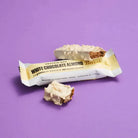 Barebells White Chocolate Almond protein bar, unwrapped and bitten, showing the white coating and brown core.