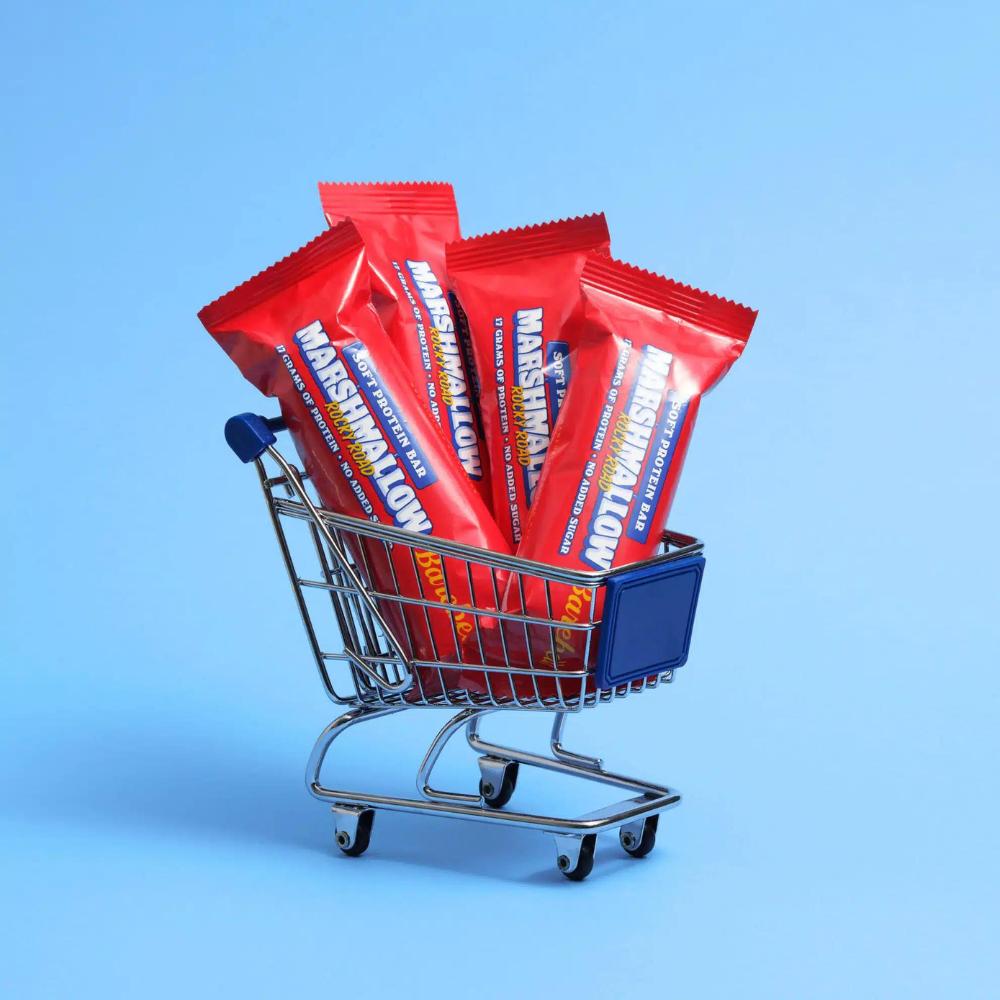 Mini shopping cart filled with four red Barebells Marshmallow protein bars against a blue background.