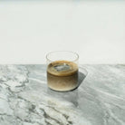 Iced hojicha latte in a clear glass on a grey marble surface.