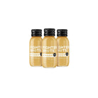 Three small, clear glass bottles of Fighter Shots Ginger juice with black caps and white labels.
