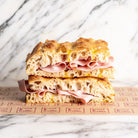 Stacked focaccia sandwich with pink Italian ham and golden crust, on branded brown paper.