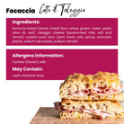 Golden focaccia bread sandwich with pink cotto ham and creamy Taleggio cheese, stacked on branded paper.