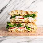 Freshly baked focaccia sandwich with sliced turkey, egg mayo, tomato, and lamb's lettuce on branded paper.
