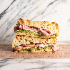 Focaccia Nutty Ham sandwich with mortadella, ricotta, and pistachio pesto on marble.