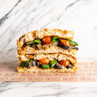 Vegan aubergine focaccia sandwich with roasted tomato hummus, cherry tomatoes, and fresh basil.