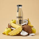 Creamy tropical smoothie in a clear glass bottle surrounded by fresh apples, pineapple slices, bananas, and coconuts.