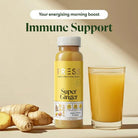 PRESS Super Ginger Juice bottle and glass with fresh ginger roots and lemon slices.