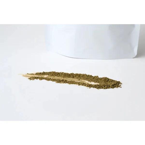 Marna Hojicha 250gm, a fine brown-green powder, spilled in a line on a white surface next to a white pouch.