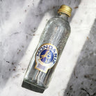 Mondariz Still Water 330ml glass bottle with gold cap and blue/gold label, lying on snow.