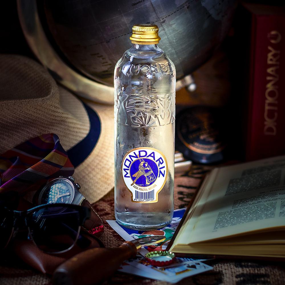Mondariz Still Water 750ml glass bottle with gold cap, blue and white label, on a rustic surface.