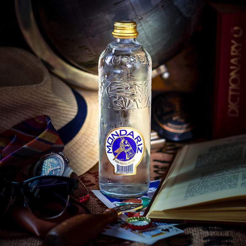 Mondariz Still Water 750ml glass bottle with gold cap, blue and white label, on a rustic surface.