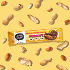 YuBi Bar Peanut Protein Bar in yellow wrapper with chocolate drizzle, surrounded by whole and shelled peanuts.
