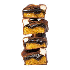 Stack of four YuBi S'Mores protein bar halves, showing gooey caramel, chocolate, and white marshmallow pieces.