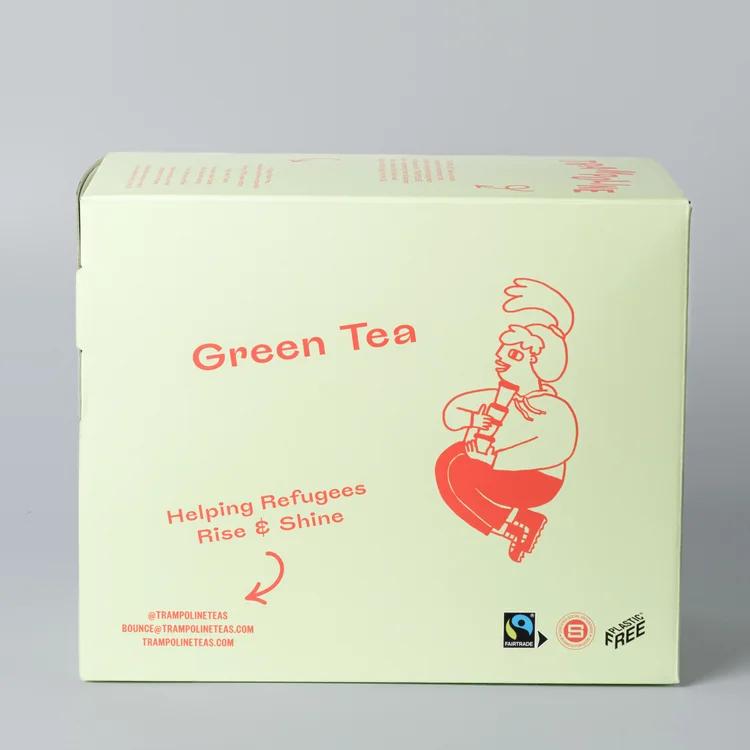 Light green box of Trampoline Green Tea, featuring a red cartoon character and "Helping Refugees Rise & Shine.