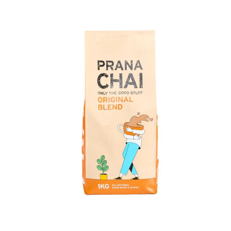 Prana Chai Original Blend 1kg bag, beige with orange base, featuring a person holding a chai cup and a plant.