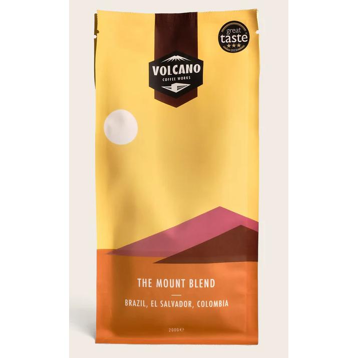 Volcano Coffee Works The Mount Blend coffee bag with yellow, brown, and orange mountain design.