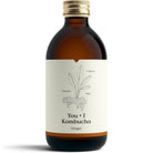 YOU + I Ginger Kombucha in a dark amber glass bottle with a gold cap and white label featuring ginger plant illustration.