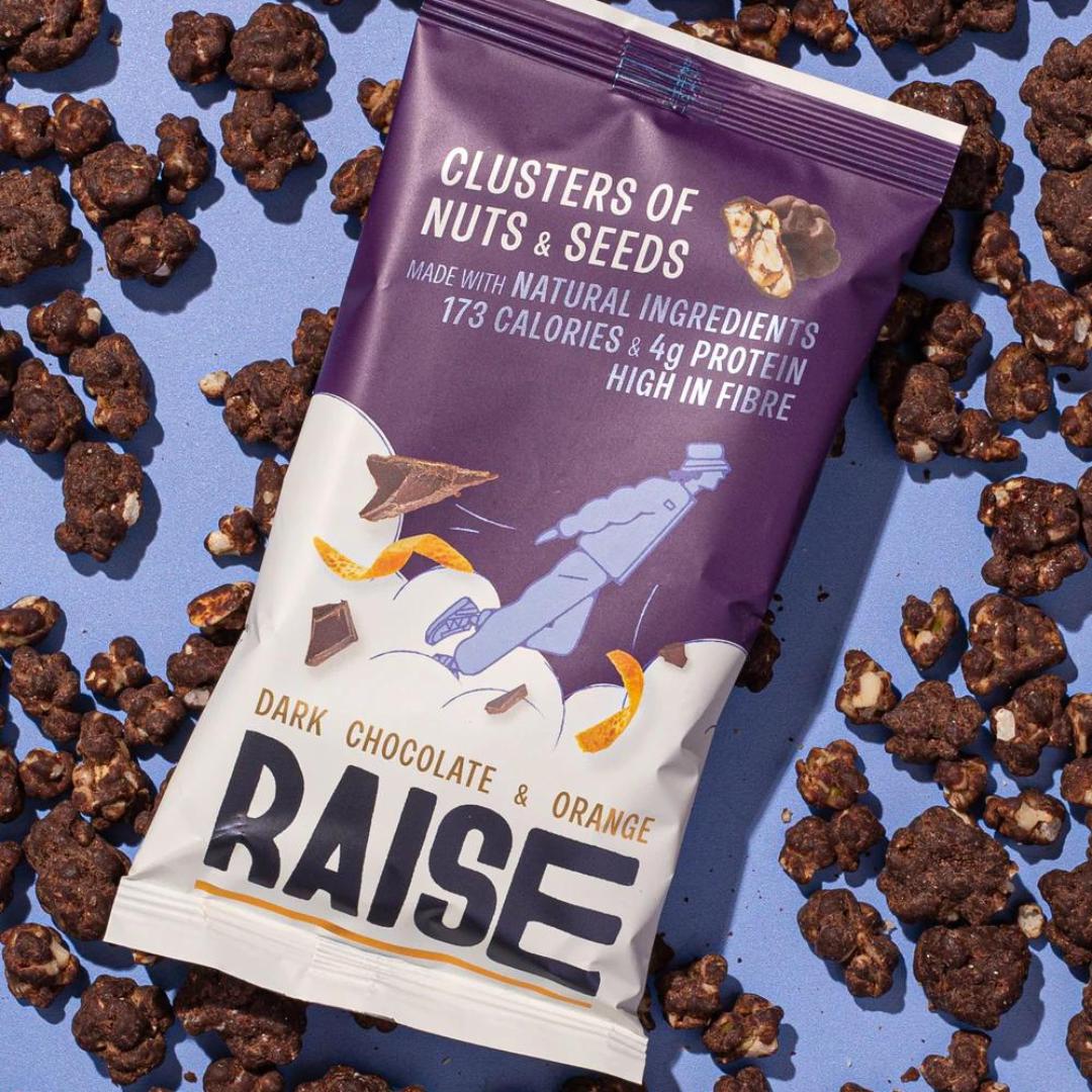 Raise Snacks Dark Chocolate & Orange Zest pouch, purple and white, surrounded by chocolate nut clusters.