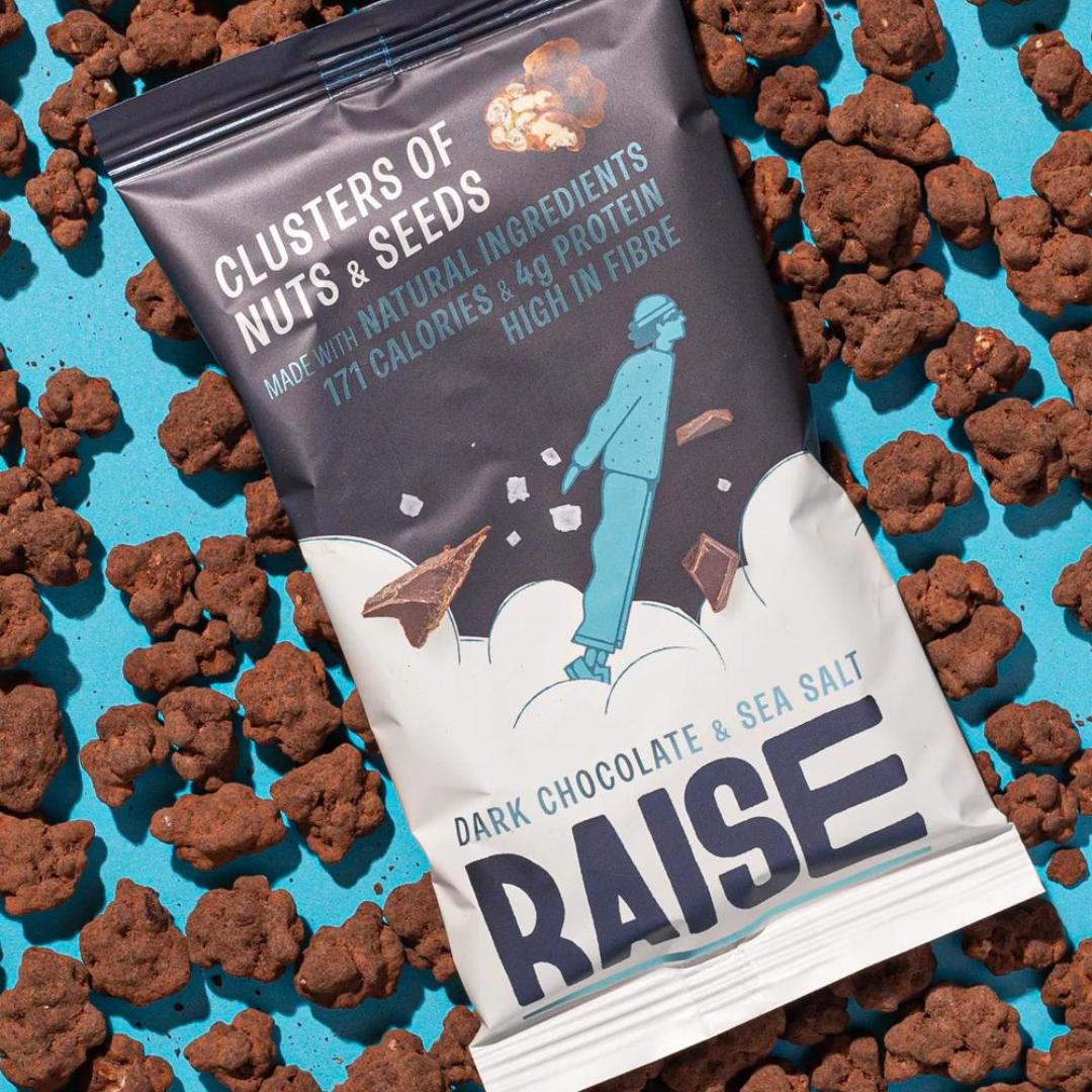 Raise Snacks Dark Chocolate & Sea Salt clusters pouch on a blue background with scattered chocolate bites.